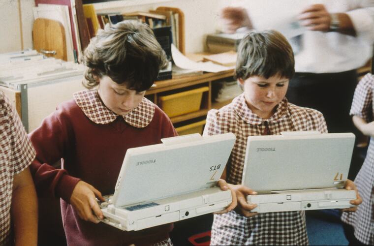 Two young girls in school uniform with laptops.