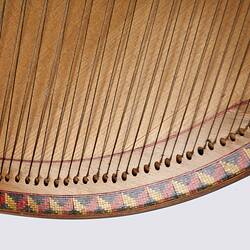 Detail of the base of a timber stringed instrument. Pale wood with black laquered timber detail. Multi stringed.