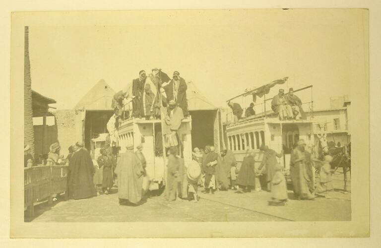 Men standing on and next to two stationary tram cars.