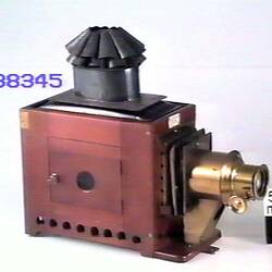 Brown box shaped projector. Brass lense at right. Black funnel on top. Side door.