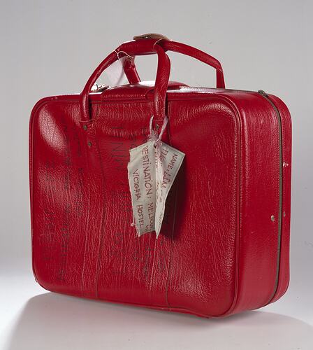 Red vinyl suitcase with luggage tag.