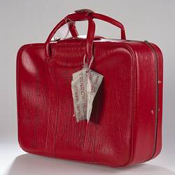 Red vinyl suitcase with luggage tag.
