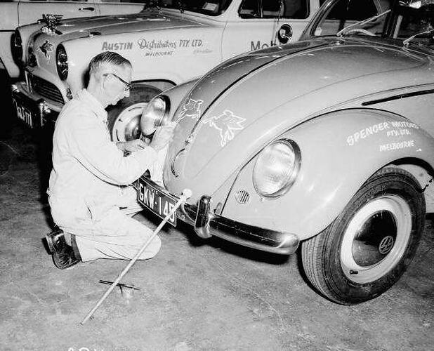 Signwriter painting Mobil `flying horse' symbols onto the bonnet of a Volkswagen motor car.