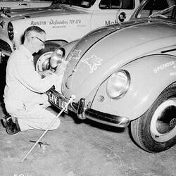 Signwriter painting Mobil `flying horse' symbols onto the bonnet of a Volkswagen motor car.