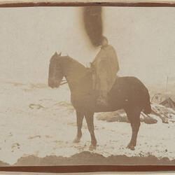 Man on horseback in snow covered landscape, damage to photograph in top centre.