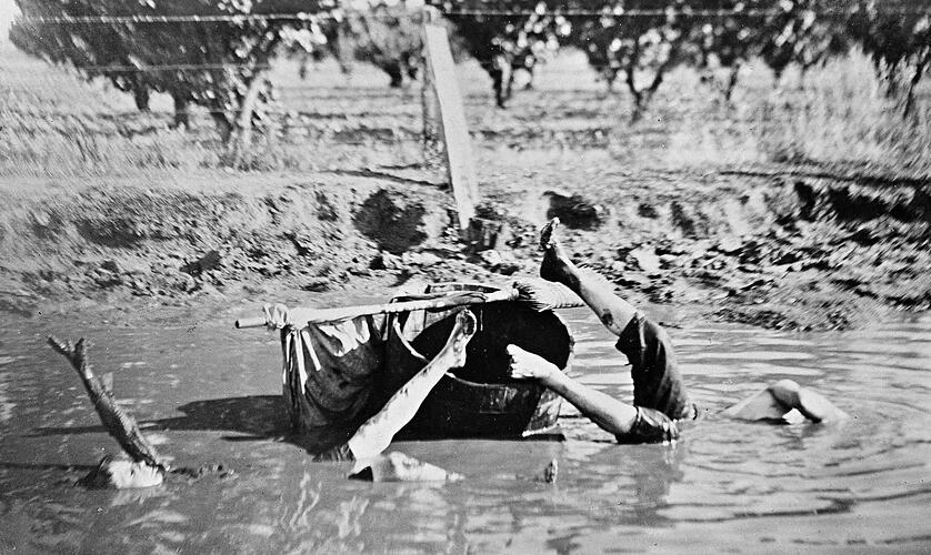 Two boys falling from a barrel into a water hole. They are partially submerged.