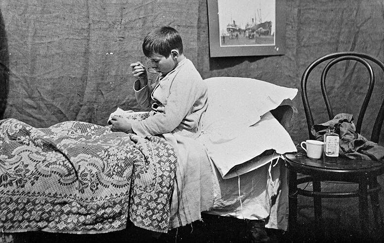 A boy, in bed, eating from a bowl.