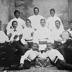 Standing and seated group of men with faces painted black. Two boys partially lay in foreground.