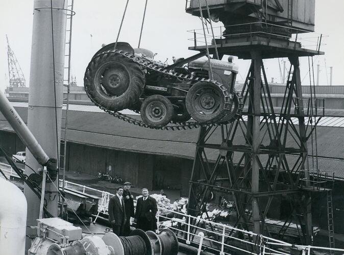 Tractor with caterpillar tracks being unloaded at docks.