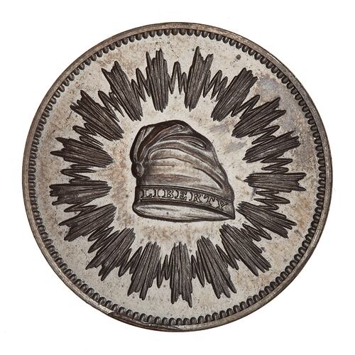 Silver medal with central cap framed by radiating lines.