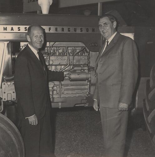 Two men standing beside a tractor.