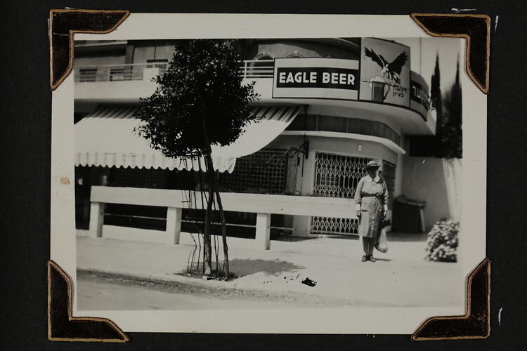 Woman standing in front of building, with small tree on left.