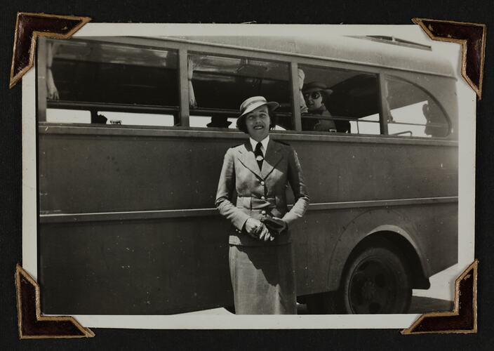 Woman in uniform standing in front of bus, another woman visible in bus window.