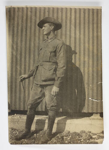 Soldier standing against corrugated iron wall holding stick.