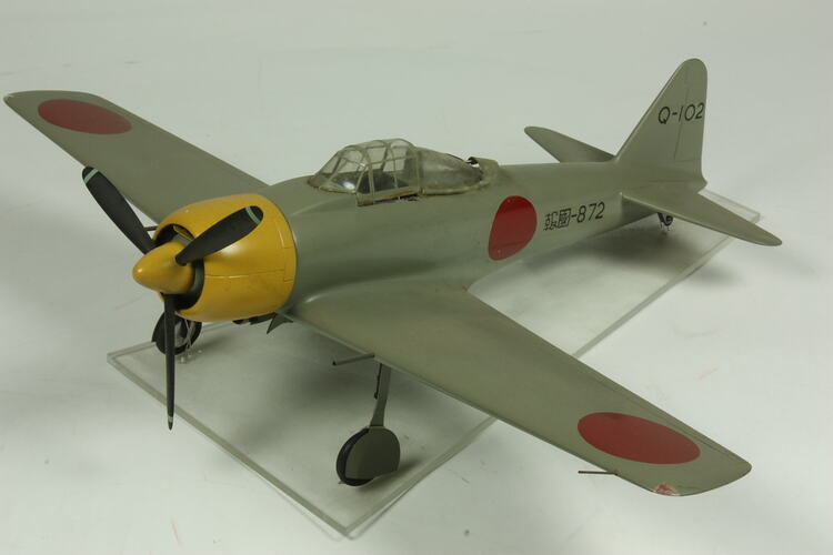 Green grey plane model with red spot on each wing and fusleage. Yellow nose, black propeller.