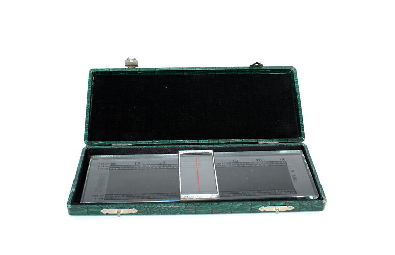 Rectangular box open, black velvet lid. Contains thick glass measure with black printed centimetres. Vertical