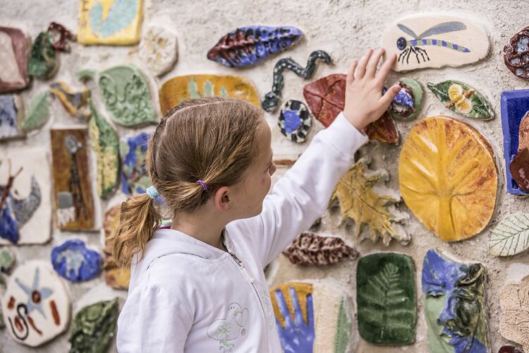 Girl reaching up to touch coloured tile wall.