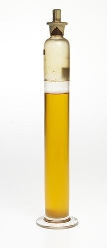 Cylindrical glass jar with yellow liquid. Two labels affixed, sealed at top.