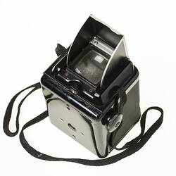 Black plastic box camera, black shoulder strap. Metal pop up viewfinder hood on top.