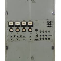 Grey metal cabinet, four closed doors. Central section has dials, switches, gauges.