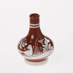 Miniature brown ceramic vase. Features white painted bird and patterns.