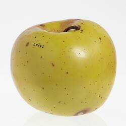 Wax model of an apple painted yellow. Has brown stem and some brown spots.