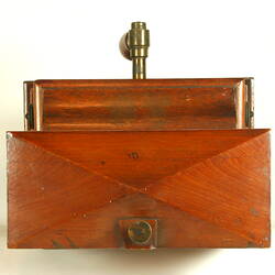 Wooden cabinet viewed from above. Brass dial on top. Brass fixture connects wooden handle.