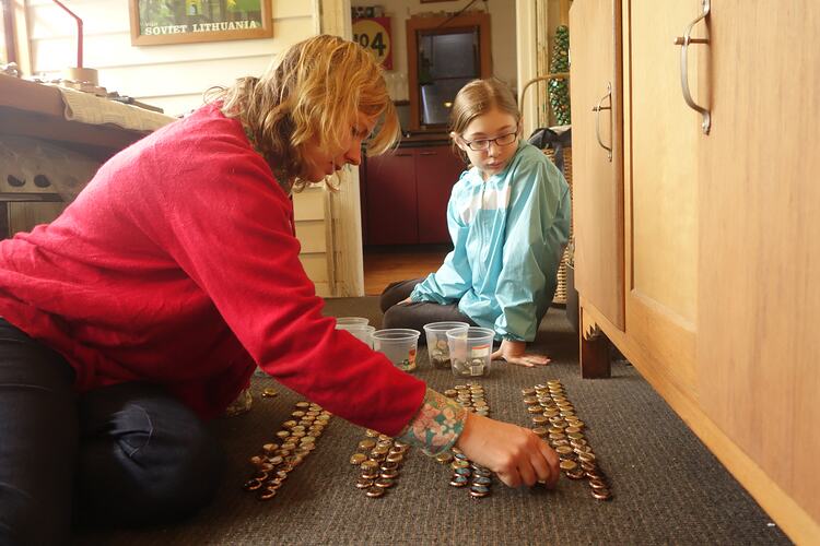 Girl and woman sitting on floor lining up bottle tops.