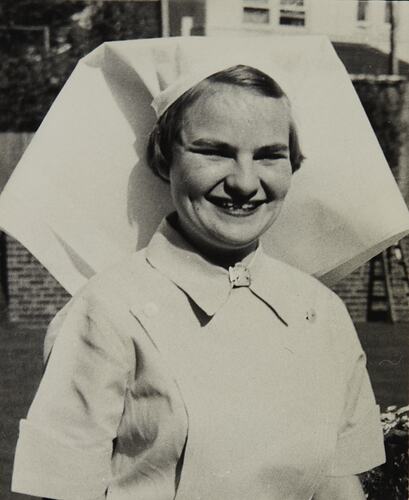 Young smiling woman wearing a nurses' uniform that includes a veiled cap, buttoned collar and pinafore.