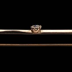 Profile of gold bar brooch with three gemstones. Purple amethyst at left end, diamond in centre and light green peridot at right end.