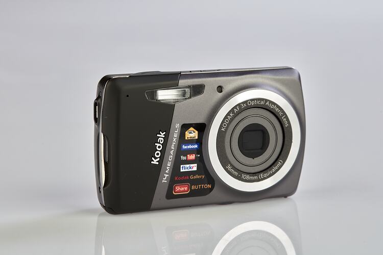 Black and grey camera with metal trim on back, sides and around the lens. Three quarter view.