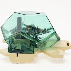 Plastic computerised turtle toy. Clear green body shell above fawn base with two red light 'eyes'. Right view.