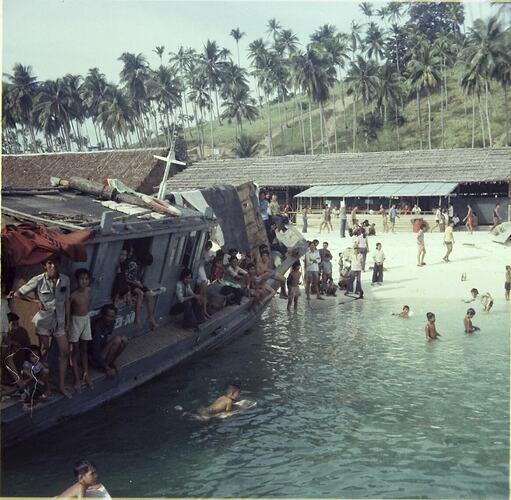 Crowded boat moored at the beach of a Vietnamese Refugee Camp. Heavily treed hill in background.