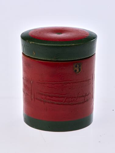 Red painted, cylindrical wooden box. Dark green trim around lid and base.