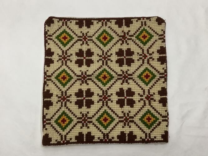 Calico cloth embroidered and cross stitched with traditional patterns in brown, green, yellow and red threads.