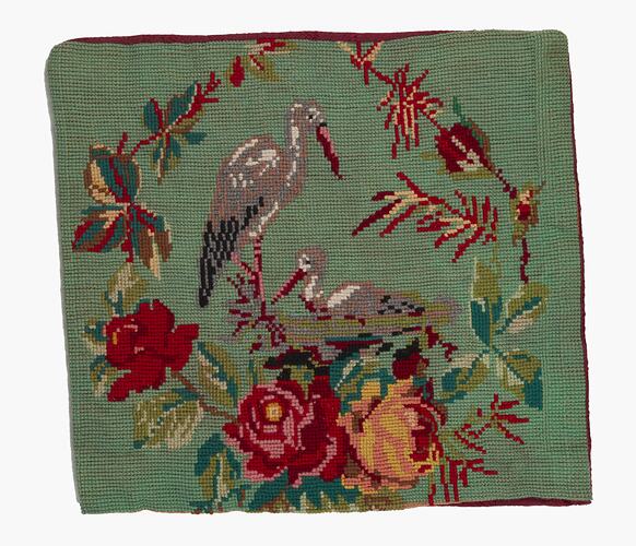 Green square cushion cover stitched with grey storks and red, yellow, green flowers design.