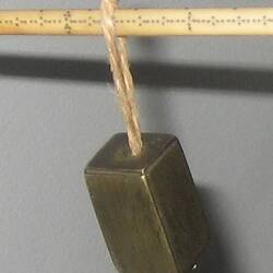 Ivory rod marked with lines. Rectagular brass weight hangs at one end and metal dish suspended from other end.