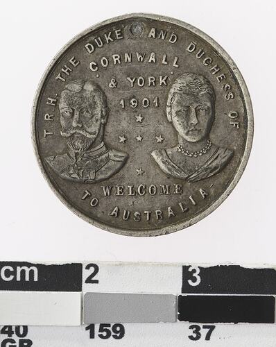 Round silver coloured medal with profile of man and woman and text surrounding,