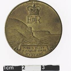 Round medal with crown and initials above coastal scene and text below.
