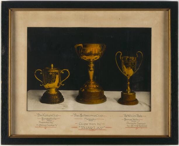Three trophies in black and gold frame. Text below photograph.
