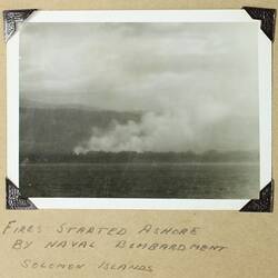 Fire and smoke on land, water in foreground.
