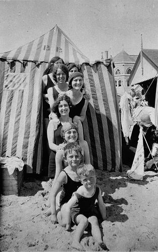 Group at beach in front of striped tent.