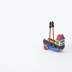 Small toy wooden boat painted blue, black, yellow and red, with three small wheels.