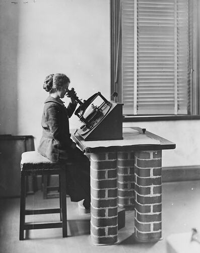 Profile of seated woman at desk with brick column legs using astrograph plate.