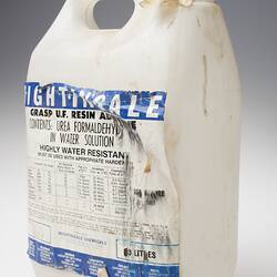 White dirty plastic bottle, white tape instead of lid. Damaged white label has blue and black printing.