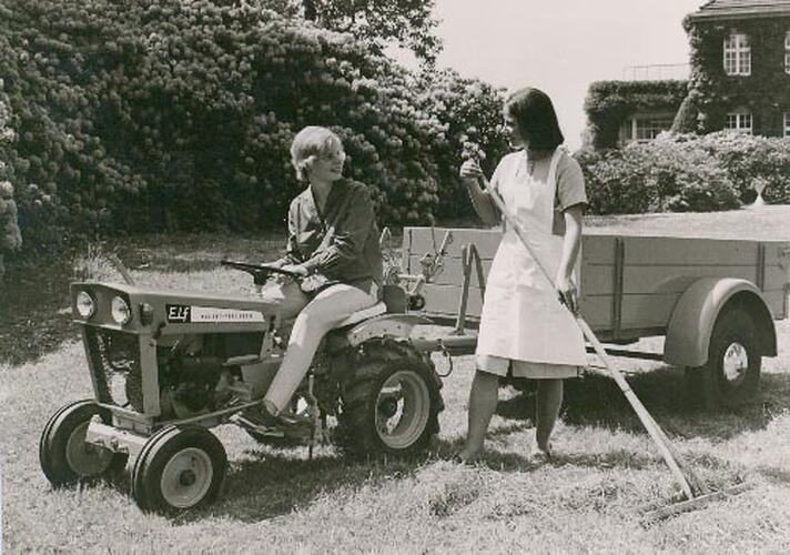 Two women with tractor and trailer in field.