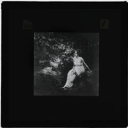 Black and white photograph of a girl in white dress next to a wattle tree.