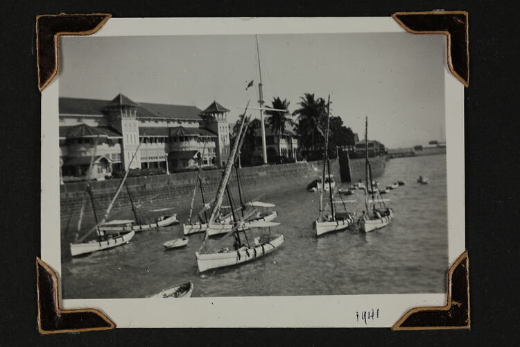 Group of boats in harbour, with wall and buildings behind.