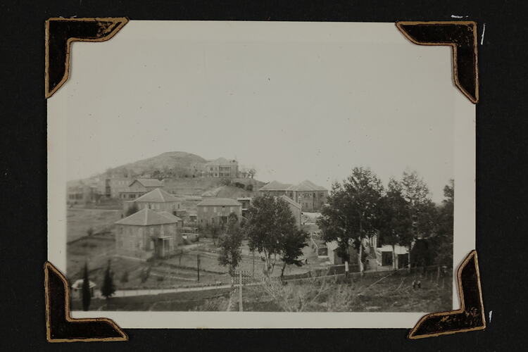 Houses on hillside, trees in right foreground.