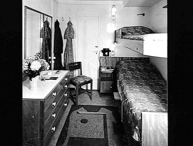Ship interior. Single bunk beds at right against wall. Chest of drawers at left.